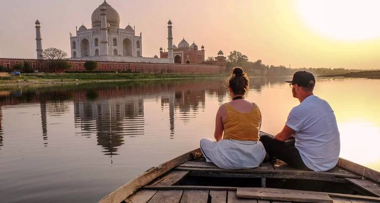 Des personnes dans un bateau sur une rivière avec le Taj Mahal en arrière-plan au coucher du soleil.
