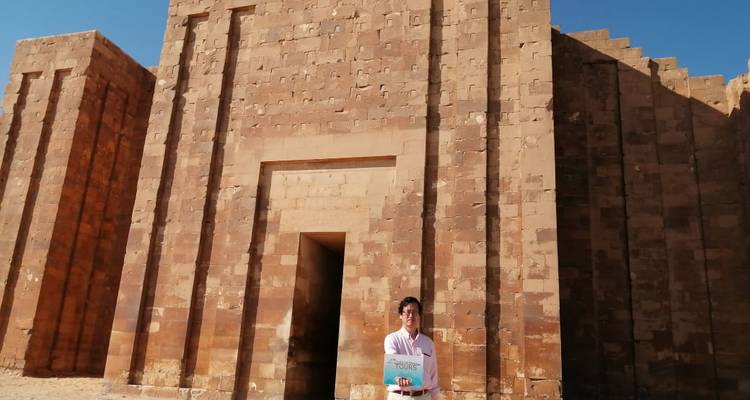 Tourist posing in front of an ancient facade with a sign.