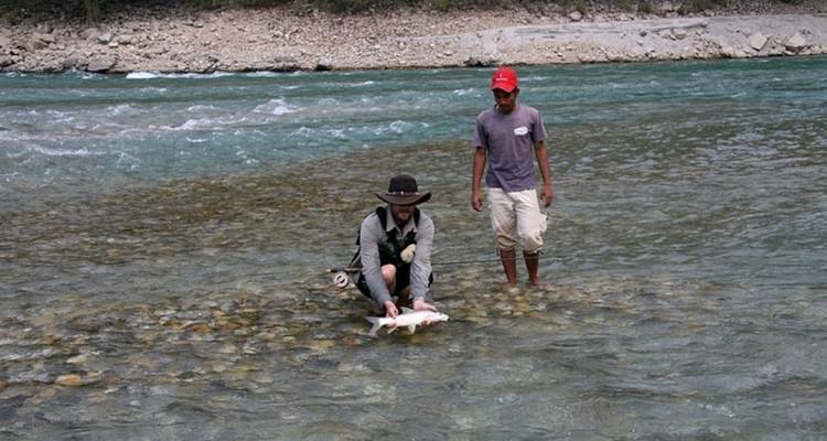 Two men fishing in a shallow, rocky river.