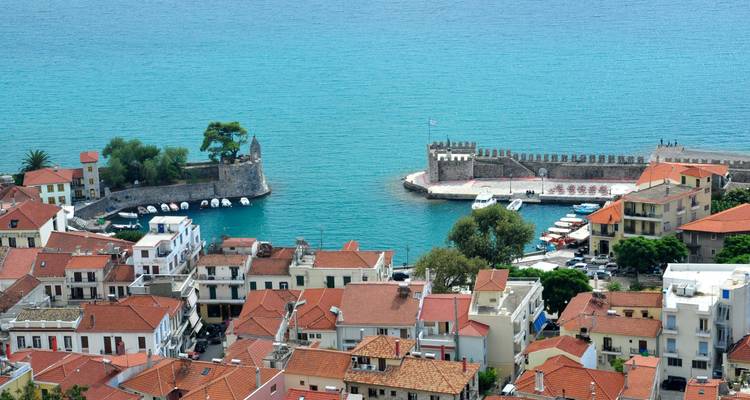 View of a coastal town with a fortress and red-tiled buildings by the sea.