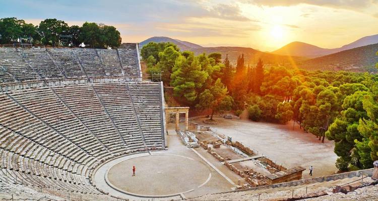 Ancient amphitheater at Epidaurus with a scenic sunset, surrounded by forests.