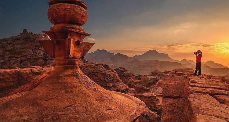 Person, die bei Sonnenuntergang auf einer felsigen Klippe ein Foto macht.