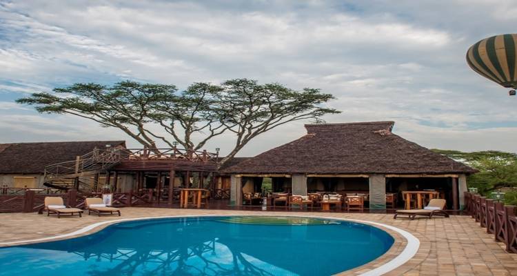 Lodge with a pool under a large tree with scenic sky.