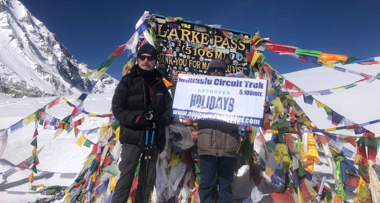 Los excursionistas posan en el letrero cubierto de nieve del Paso Larke adornado con banderas de oración en el Himalaya.