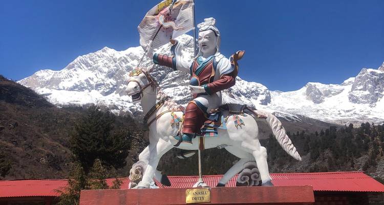 Estatua colorida de guerrero a caballo situada ante picos nevados del Himalaya y cielo azul.