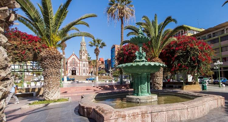 Ein Stadtplatz mit einem Brunnen und einer Kirche im Hintergrund.