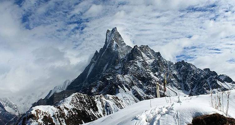 Schneebedeckter Berg mit Fußspuren im Vordergrund unter einem bewölkten Himmel.