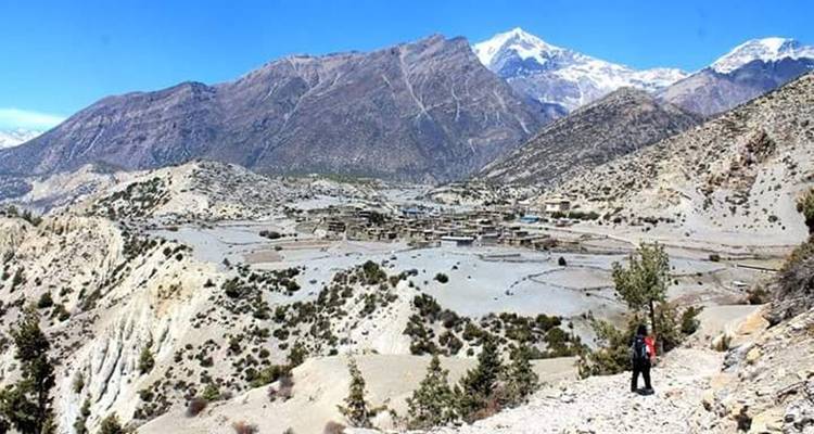 Dorf inmitten rauer Landschaft mit Bergkulisse und einem Wanderer.