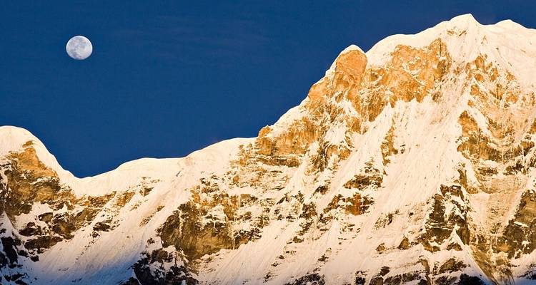 Moon rising over snow-covered mountain peaks.