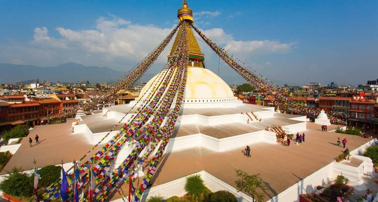 Large stupa with prayer flags and crowds around it.