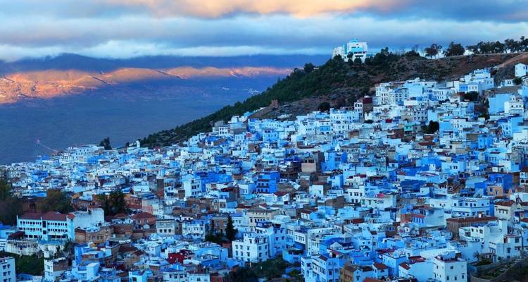 Pueblo en la ladera con edificios pintados de azul y un telón de fondo montañoso.