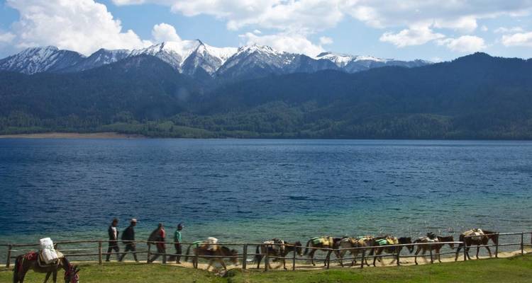 Meer met bergen en mensen met pakdieren aan de waterkant.