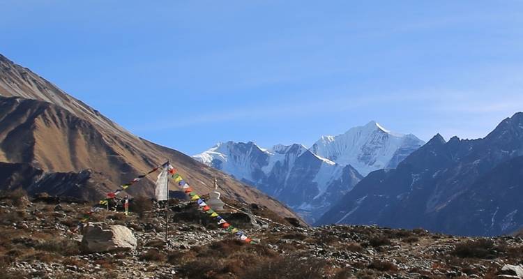 Mountainous terrain with prayer flags and blue sky.