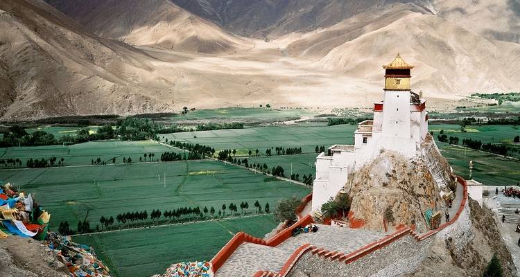 Dzong overlooking green fields and mountains in Tibet.