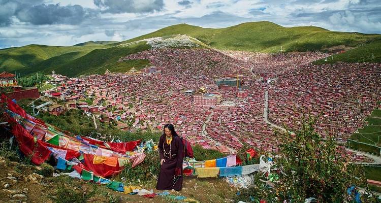 View over a Tibetan monastery town with prayer flags and hills in the background.