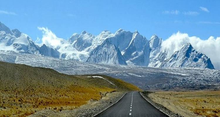 Road leading to distant snowy mountains under a blue sky.