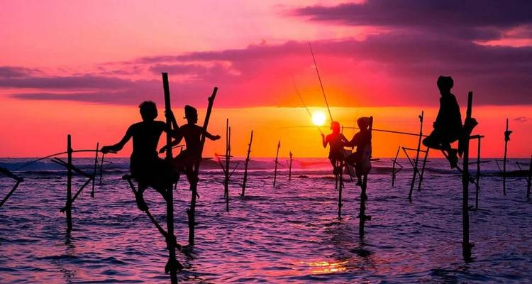 Pescadores en silueta sobre zancos al atardecer en el océano.