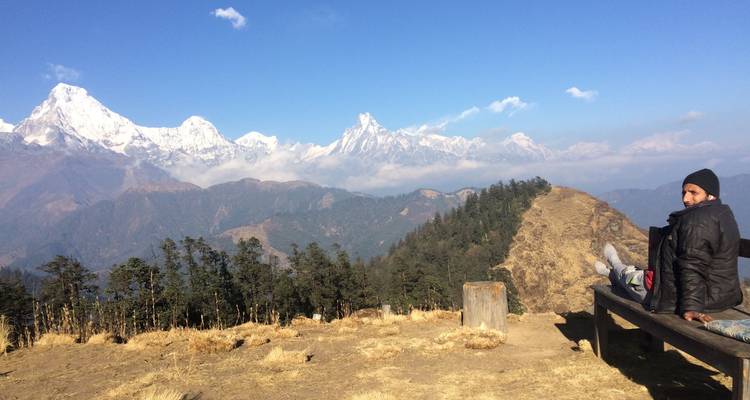 Persoon zittend op een bank met uitzicht op een bergketen.