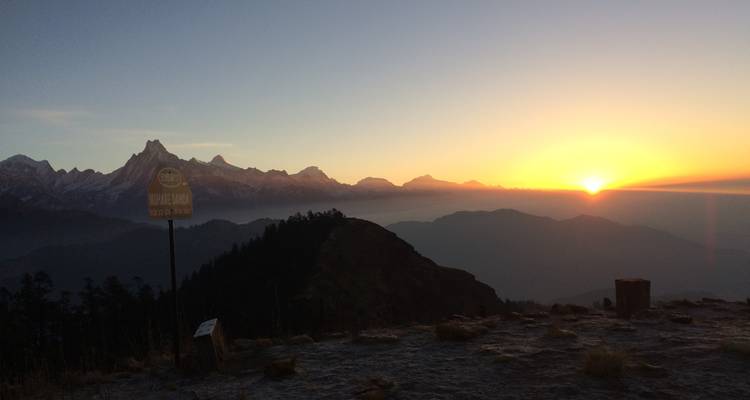 Zonsondergangzicht met bergen en een bord voor Mohare Danda.