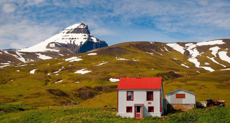 Picturesque house with a red roof in front of a snow-capped mountain.
