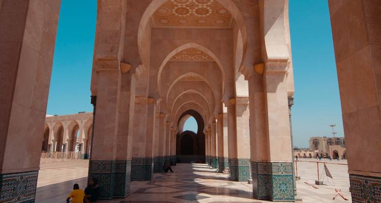 Binnenarcade van de Hassan II-moskee met sierlijke bogen, tegeltwerk en bezoekers die in de schaduw uitrusten.