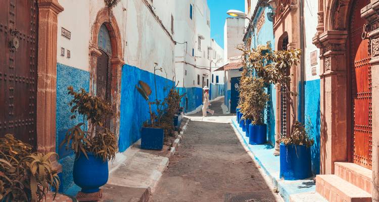 Stille blauwe en witte steeg in Rabat's Kasbah met potplanten en een eenzame wandelaar.