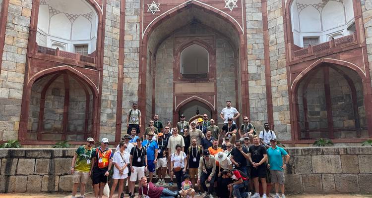 Un gran grupo de personas posando frente a un edificio histórico con arquitectura de arenisca roja.