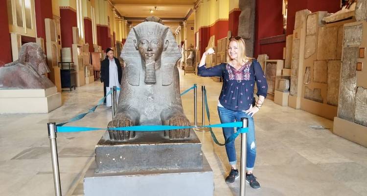 Woman posing next to a sphinx statue in a museum.