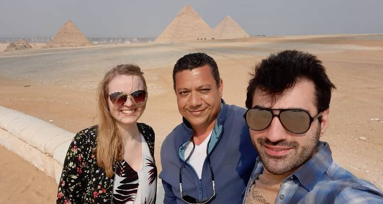 Group photo with three people smiling in front of pyramids.
