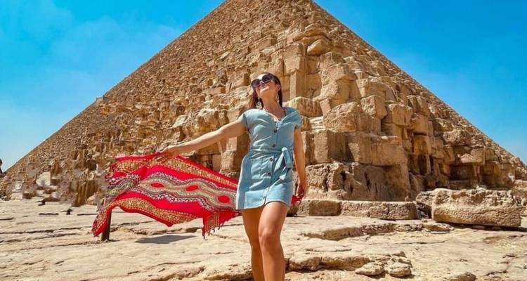 Woman posing in front of a pyramid with a colorful scarf blowing in the wind.