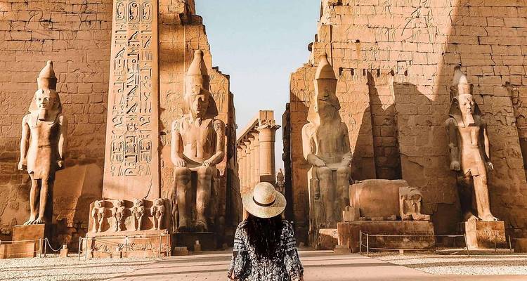 A person walking towards massive ancient statues and hieroglyphics.