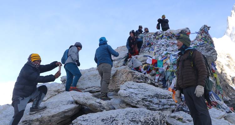 Groupe de randonneurs au sommet rocheux avec drapeaux de prière.