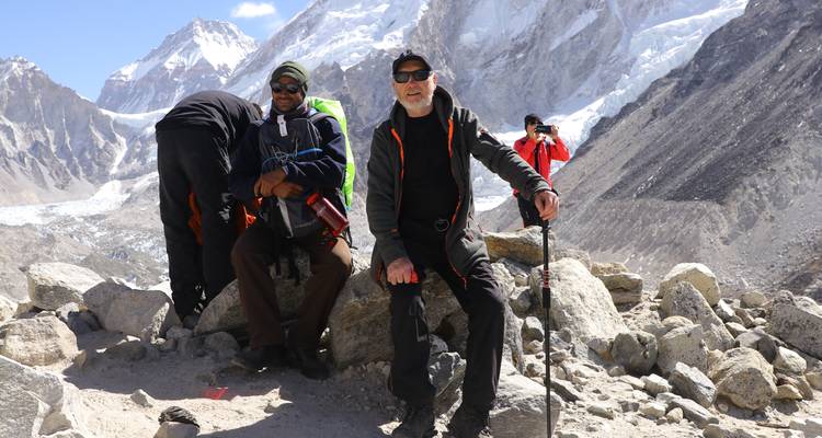 Groupe de randonneurs posant sur un terrain rocheux avec des pics enneigés en arrière-plan.