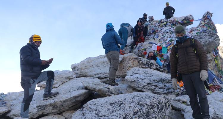 Groupe de randonneurs se reposant sur un sommet rocheux avec des drapeaux de prières.