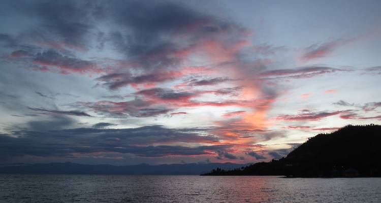 Panorama de una puesta de sol sobre una gran masa de agua y colinas.