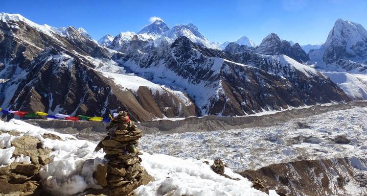 Montículo de piedras con banderas de oración coloridas con vista a montañas nevadas.