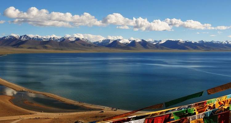 Scenic view over a large lake with mountains in the background and prayer flags on the side.