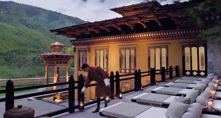 Person in traditional attire lighting lanterns on a terrace of a beautiful Bhutanese building.