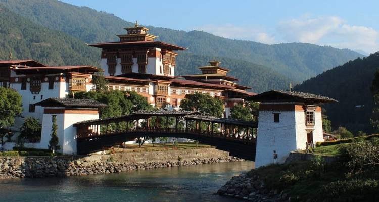 Punakha Dzong with a traditional bridge spanning a river, surrounded by mountains.