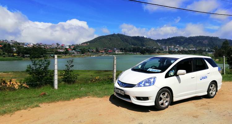 Car parked by a fence with a lake and township in the background.