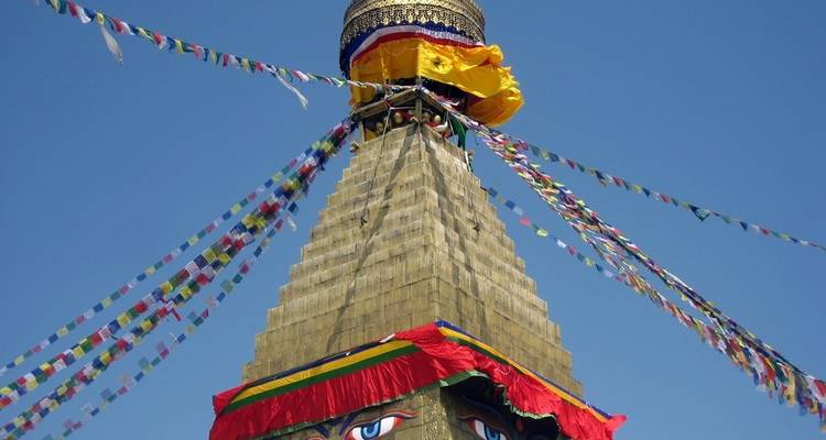 Top of a stupa with prayer flags and a clear blue sky.