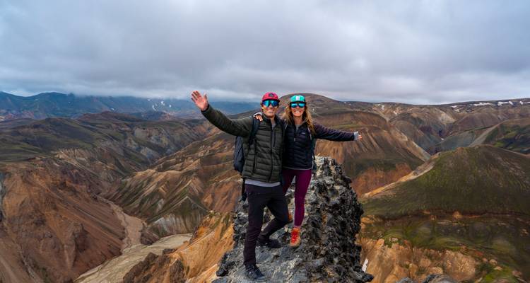 Un couple aventureux se tient sur un étroit piton rocheux haut au-dessus des vallées colorées de Landmannalaugar.