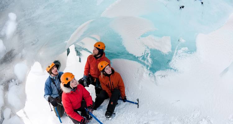Des aventuriers casqués se reposent à l'intérieur d'une grotte de glace entourée de parois glaciaires turquoise.