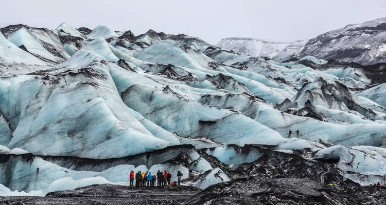 Petit groupe éclipsé par les imposantes crêtes de glace bleue d'un glacier islandais.