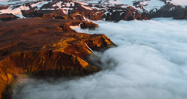 La luz dorada baña acantilados escarpados que se elevan sobre un océano de nubes en una vista aérea.