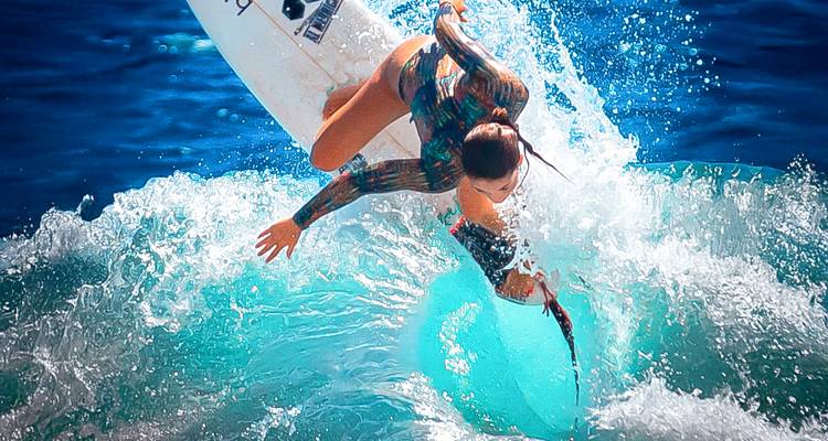 Action shot of surfer performing maneuver on turquoise wave in bright sunlight