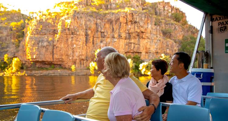Group of people on a boat tour viewing a cliff face at sunset.
