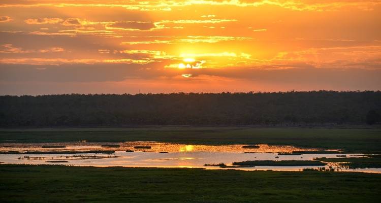 Vibrant sunset over wetlands with reflection in water.