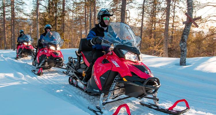 Los pilotos conducen motos de nieve de color rojo brillante por un sendero nevado en el bosque bajo la clara luz solar del invierno.
