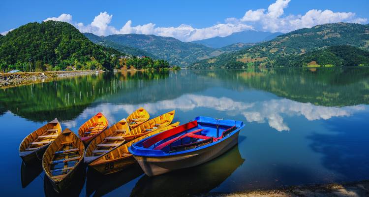 Boten op een serene meer met bergachtergrond, waarschijnlijk het Phewa-meer in Pokhara.